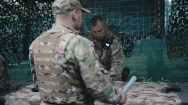 Komutan ve üniformalı yardımcısı işbirliği içinde dışarıda bir görev planlıyor. Komutan ayrılır, asistan bir harita hazırlar ve stratejiyi tartışırlar..