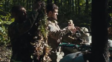 İki asker üniformalarını güneşli bir günde ormanda savaşa hazırlıyor..