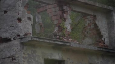 Tetikte, maskeli ve silahlı bir asker, yıkılmış bir evin balkonunda bekliyor..