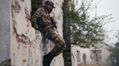 İki asker takım çalışması sergiliyor. Biri yıkılmış bir evin penceresinden atlıyor, diğeri de arkasını kolluyor. Askeri tatbikata katıldıklarında, doğal bir açık hava ortamında koordinasyon gösterirler..
