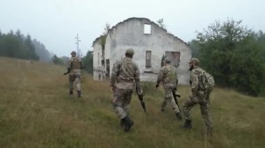 Askeri üniforma giymiş dört profesyonel asker, savaştan zarar görmüş bir evin kırsal kesiminde yürüyorlar. Sis onların manzarasını sarıyor..