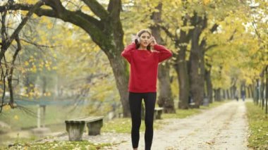 Aktif genç kadın dışarıda koşuya ara veriyor, akıllı telefonu kontrol ediyor, gülümsüyor ve koşuya devam ediyor. Sonbaharda sağlıklı bir rutin sırasında spor, teknoloji ve doğayı kucaklamak.