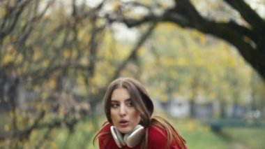 Genç bayan koşucu dışarı çıkmak için koşuya ara veriyor, kulaklıklarını çıkarıyor, telefonlarını kontrol ediyor, kulaklıklarını takıyor, gülümsüyor ve koşuya devam ediyor. Sonbaharda spor, teknoloji ve doğa.