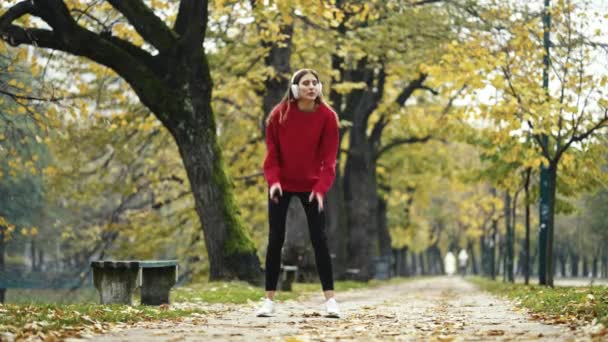 アクティブな若い女性は屋外に伸びるためにジョギングを一時停止し スマートフォン 笑顔をチェックし ジョギングを続けます 秋の健康的なルーチン中にフィットネス 自然を取り入れる — ストック動画