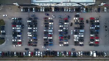 Kalabalık bir şehir manzarasında, alışveriş merkezinin dışındaki kalabalık bir otoparkta arabalar geziniyor. Tepeden tırnağa perspektif bu hareketli perakende merkezinde şehir hayatının ve tüketiciliğin enerjisini yakalıyor..