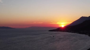 Adriyatik Denizi üzerinde bir Hırvat gün batımının alçalan görüntüsü. Turuncu renkler, kıyı ufkunun üstündeki gökyüzünü boyuyor Dalmaçya 'da romantik ve huzurlu bir atmosfer yaratıyor..