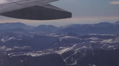 Karlı dağ manzaralı kış yolculuğu bir uçaktan diğerine uzanır. Alp manzarası pencereden görülebiliyor, maceranın özünü ve yüksek irtifa panoramasını yakalıyor..