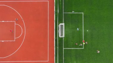 Çocuklar bitişik tarlalarda basketbol ve futbol oynarlar. Havadan yukarıdan aşağıya bakış, aktif çocukluğun özünü yakalar, eğlence, eğlence ve takım sporları açık hava ortamında bir araya gelir..