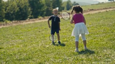 On a sunny day in nature, a playful scene unfolds as a young Caucasian boy and girl engage in leisure. Boy is missing the shuttlecock.