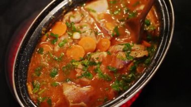 A traditional Balkan dish comes to life as skilled hands stir vegetables and meat with a wooden spoon on the hot stove. This homemade culinary delight features ingredients like carrots and parsley.