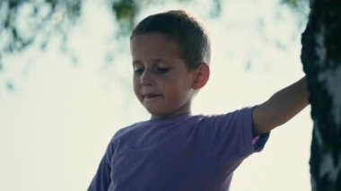 Mor tişörtlü çocuk doğa gölgesinde duruyor. Sarışın, Kafkasyalı ve masum olan Bosnalı çocuk, Balkanlar 'da bir yaz günü açık havada eğleniyor.