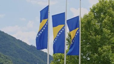 Bosna-Hersek bayrakları Srebrenica Anma Merkezi önünde yarıya indirilirken, arka planda doğa görülüyor. Soykırım kurbanlarını hatırlama, yas tutma ve onurlandırma kavramı.