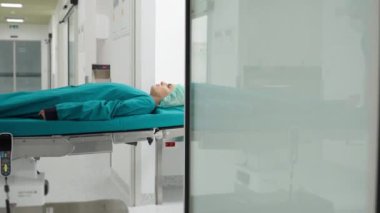 Kadın bir hastayla birlikte bir hastane sedyesini temiz bir tıbbi koridorda iten sağlık görevlisi sakin ve steril bir ortam sergiliyor. Sağlık ve tıbbi ulaşım kavramı.