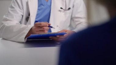 Klinikteki hasta muayenesi sırasında beyaz önlüklü doktor panoya notlar yazar. Tıbbi belgeler, profesyonel bakım, sağlık hizmetleri iletişimi ve teşhisi