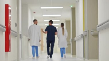 Hastane koridorunda ağır çekimde yürüyen tıp uzmanları, sağlık ortamında takım çalışması ve işbirliği sergiliyorlar. Modern tıp uygulaması kavramı.