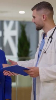 Dikey Ekran: Bir kadın müşteri ile bir erkek doktor arasındaki profesyonel etkileşim modern bir tıbbi tesiste kameraya doğru dönüyor, el sıkışma sırasında kaydedildi. Güven kavramı, sağlık hizmeti.