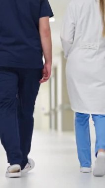 Dikey Ekran: Parlak bir hastane koridorunda yürüyen sağlık görevlileri, ekip çalışması ve profesyonellik sergiliyorlar. Tıbbi personel kavramı, sağlık hizmetleri işbirliği, modern hastaneler.