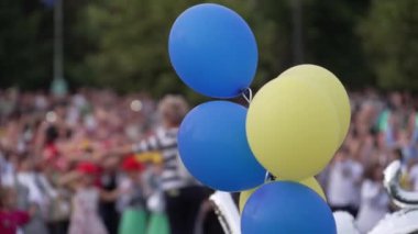 Okula dönüş etkinliğinde mavi ve sarı balonlar, arka planda bulanık bir aile ve çocuk kalabalığı. Eğitim anlayışı, yeni başlangıçlar ve topluluk kutlamaları.