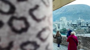 Mostar, Bosna - 1 Ocak 2025: Mostar 'daki ikonik Eski Köprü manzarasının keyfini çıkaran turistler, market tezgahları ve yerel zanaatlarla çevrili. Kültürel turizm ve miras keşfi kavramı.