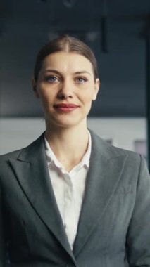 Modern bir ofis koridorunda duran, resmi gri bir takım elbise giyen ve kolları bağlı gülümseyen kendine güvenen bir iş kadını. Profesyonellik, liderlik, kurumsal başarı kavramı.