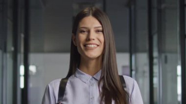 Kendine güvenen genç bir kadın gülümserken başını sallıyor modern bir ofis koridorunda cam duvarlarla dikiliyor. Anlaşma, olumluluk ve mesleki güven kavramı.