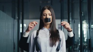 Ofis koridorunda ağzı bir erkeğin elleriyle bantlanmış bir şekilde duran genç profesyonel bir kadın sansür veya işyeri eşitsizliğini sembolize ediyor. Baskı ve susturma kavramı.