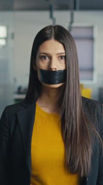 Profesyonel kadın ağzındaki koli bandını çıkartıyor, modern ofis ortamında sessizlikten güçlenmeye geçiyor. Kendini ifade etme kavramı, işyeri hakları, güçlendirme.