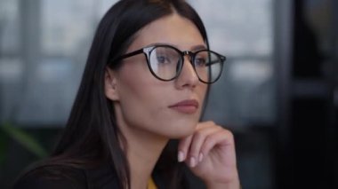 Siyah çerçeveli gözlüklü profesyonel bir kadın, modern ofis ortamında dikkati ve anlayışı ileterek onaylıyor. Profesyonellik ve aktif dinleme kavramı.