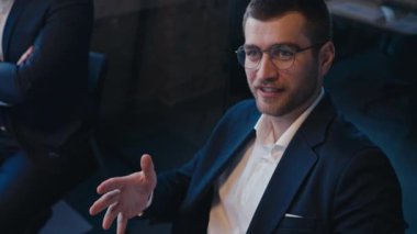 Modern bir ofis ortamında şirket toplantısı sırasında gözlüklü, hareketli ve çekici kendine güvenen bir iş adamı. İş yerinde profesyonel iletişim ve liderlik kavramı.
