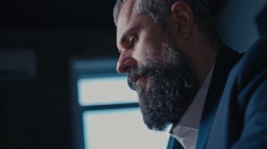Şık sakallı odaklanmış işadamı modern bir ofiste dizüstü bilgisayarla çalışıyor, doğal ışıkla aydınlatılıyor. Mesleki adanmışlık, kurumsal yaşam tarzı ve modern çalışma ortamı kavramı.