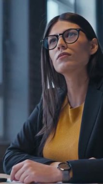 Dikey Ekran: Modern bir ofiste iş kadını gözlük takıyor ve bir tartışma sırasında dikkatlice dinliyor, anlayış ve odaklanma gösteriyor. İletişim kavramı, profesyonellik.