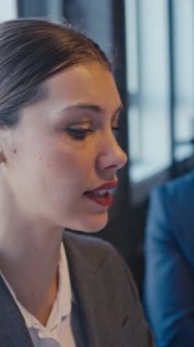 Dikey Ekran: Bir şirket toplantısında iş kadını, arka planda bir meslektaşı dinlerken fikirlerini güvenle sunuyor. Liderlik, iletişim ve takım çalışması kavramı.