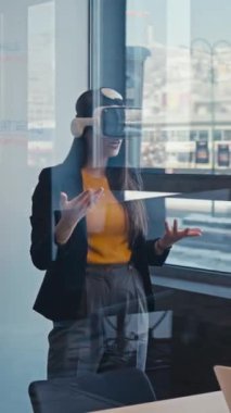 Dikey Ekran: kadın sanal gerçeklik kulaklığı takıyor ve bir ofiste konuşuyor, cam duvarlar ve modern dekorlarla çevrili, büyüleyici teknolojiyi keşfediyor. Yenilik kavramı