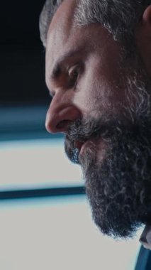 Dikey Ekran: Odaklanmış sakallı bir iş adamı modern bir ofiste dizüstü bilgisayarla çalışır, doğal ışıkla aydınlatılır. Mesleki adanmışlık kavramı, kurumsal yaşam tarzı.