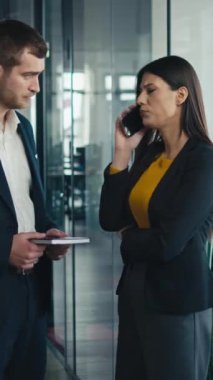 Dikey Ekran: Modern bir ofiste iş adamı ve iş kadını, ikisi de düşünceli ve endişeli görünen bir telefon görüşmesinden sonra sessizce durakladı. İş yeri stresi ve mesleki zorluklar kavramı.