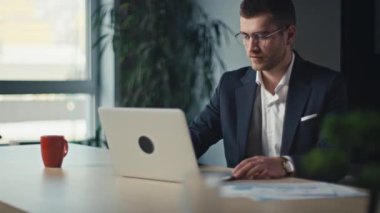 İş adamı işe gelir, bilgisayarını açar ve kahve içerken sıcak bir şekilde gülümser. Güne başlama kavramı, olumlu duygular ve mesleki alışkanlıklar.