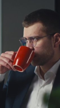 Gözlüklü, takım elbiseli, geç saatlere kadar masa başında çalışırken kahvesini yudumlayan profesyonel bir adam. Odaklanma, üretkenlik ve modern ofis yaşam tarzı kavramı.