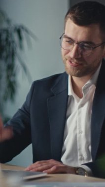 Dikey Ekran: Takım elbiseli kendine güvenen iş adamı video görüşmesini bitiriyor, gülümsüyor ve dizüstü bilgisayarına el sallıyor. Profesyonel iletişim, uzak çalışma ve modern ofis yaşam tarzı kavramı.