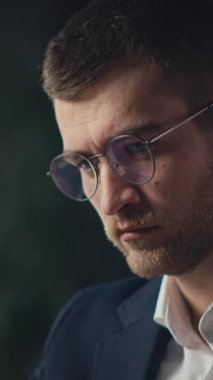Dikey Ekran: Gözlüklü düşünceli bir adam modern ofis ortamında dizüstü bilgisayarda çalışır, odaklanma ve tefekkür gösterir. İş yeri verimliliği, konsantrasyon veya karar verme kavramı.