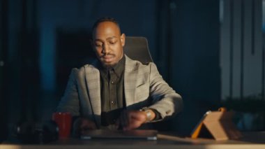 Modern bir ofisteki profesyonel Afro-Amerikan iş adamı gece geç saatlere kadar dizüstü bilgisayarıyla çalışır. Kulaklık takıyor, önemli bir göreve odaklanıyor. Bağlılık kavramı, verimlilik, uzak çalışma.