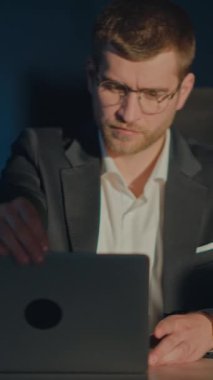 Dikey Ekran: Karanlık bir ofiste genç bir işadamı gözlük takar, laptopunu açar ve çalışırken kahve içer. Odaklanma, kararlılık, gece yarısı üretkenliği, profesyonel özveri.