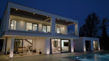 Modern lüks villa geceleri aydınlık, büyük pencereler, geniş balkonlar ve bir yüzme havuzu var. Çağdaş mimari ve açık hava yaşam tarzı kavramı.
