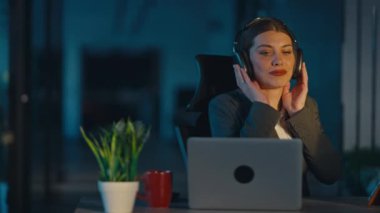 İş elbiseli genç bir kadın loş bir ofiste geç saatlere kadar çalışırken müzik dinlemekten hoşlanıyor. Birlikte şarkı söylüyor, kulaklık takıyor, rahatlama ve odaklanma gösteriyor. İş-yaşam dengesi kavramı.