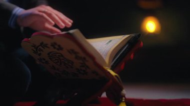 Müslüman bir adam Kuran 'ı sıcak mum ışığıyla aydınlatılmış ahşap bir rehal' de okur. Sahne ruhanilik, bağlılık ve huzurlu bir tefekkür içeriyor. İslami inanç ve dini uygulama kavramı.