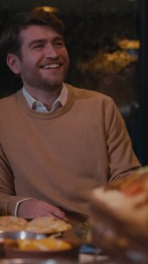 Neşeli genç adam rahat bir restoranda yemek yiyor, gülümsüyor ve sohbet ediyor. Yemek, sosyalleşme, olumlu duygular, iftar kavramı.