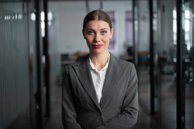 Resmi gri takım elbiseli profesyonel bir iş kadını modern ofis ortamında güvenle kameraya bakıyor. CEO, yönetici, yönetici, yönetici, asker toplayıcı, insan kaynakları, analist, avukat, bankacı..