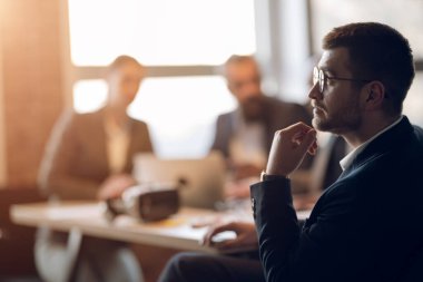 Modern bir ofiste otururken, toplantı sırasında derin düşüncelere dalan bir iş adamı. Stratejik karar verme, liderlik, kurumsal planlama ve profesyonel çalışma ortamı kavramı.