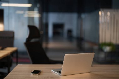 Minimalist ofis ayarları, parlak bir dizüstü bilgisayar ve ahşap bir masada akıllı telefon. Modern çalışma alanı kavramı, uzak çalışma, dijital iş, üretkenlik ve çağdaş ofis tasarımı.