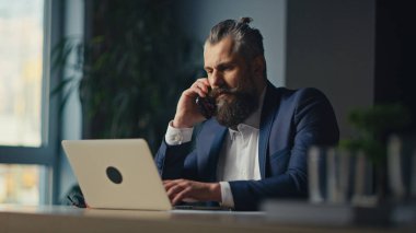 Modern bir ofiste dizüstü bilgisayarla çalışırken sakallı, olgun bir ekonomist, yönetici ya da muhasebeci konuşuyor. Liderlik kavramı, iş iletişimi ve iş ahlakı.