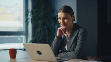 Ofisteki gülümseyen yönetici ya da danışman dizüstü bilgisayara bakıyor, çevrimiçi toplantı sırasında kendinden emin ve rahat görünüyor. Profesyonel başarı kavramı, uzak çalışma, dijital iletişim ve liderlik.